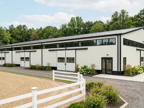 Pre-engineered steel riding arena with white walls and black trim on a rural equestrian property